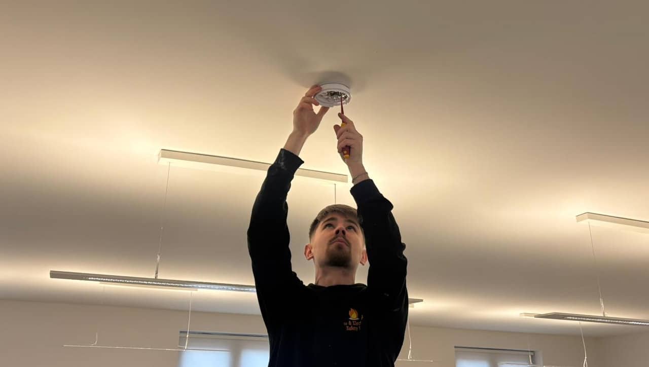 A person installs a fire alarm on the ceiling using a screwdriver.