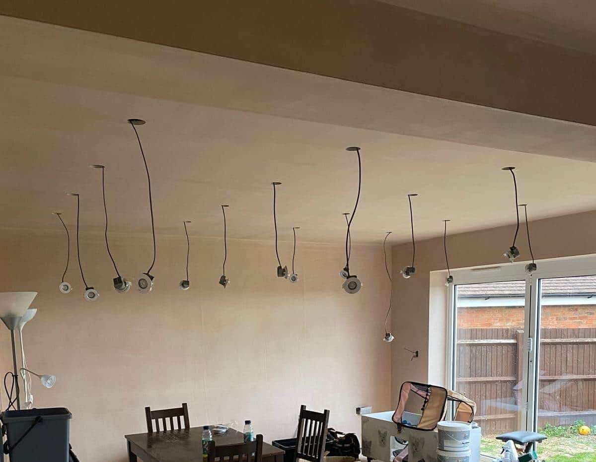 Unfinished room with ceiling lights hanging down by wires, a table, chairs, and various household items.