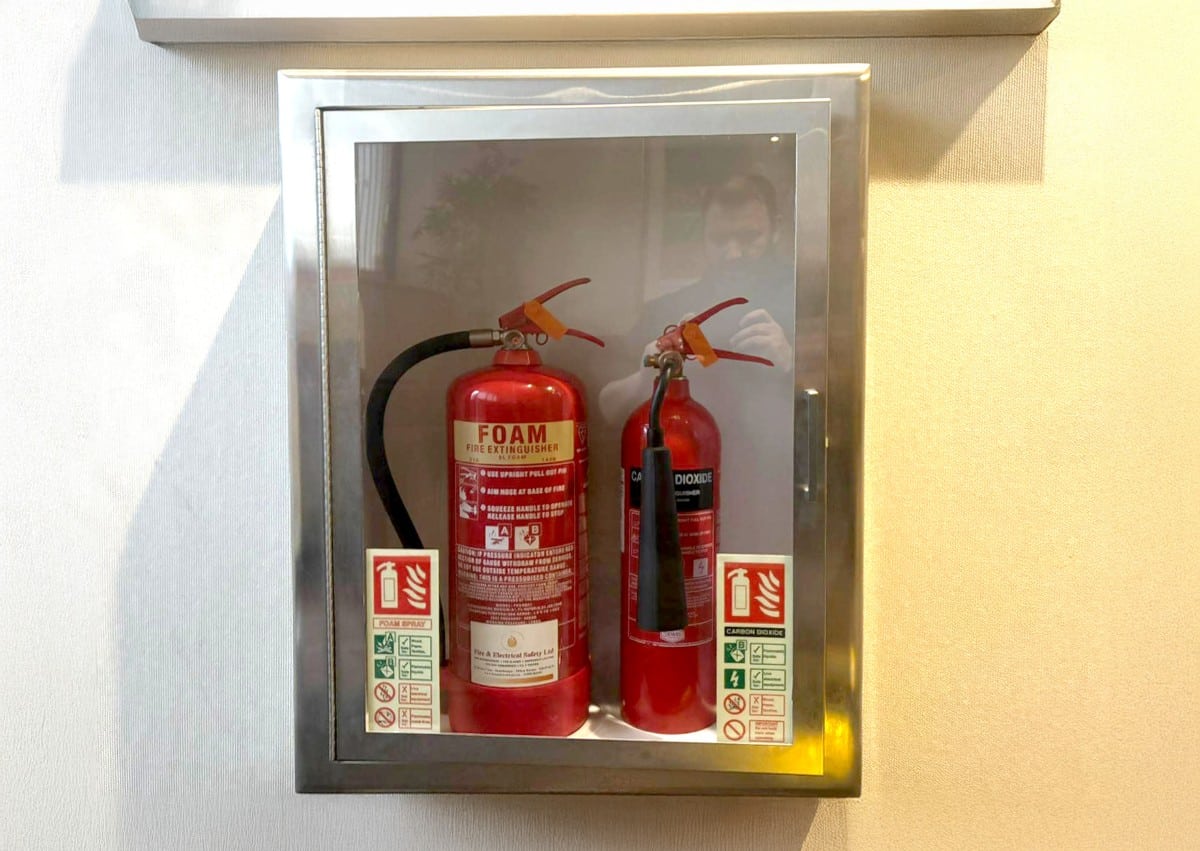 Two fire extinguishers in a wall-mounted case with safety instruction labels.