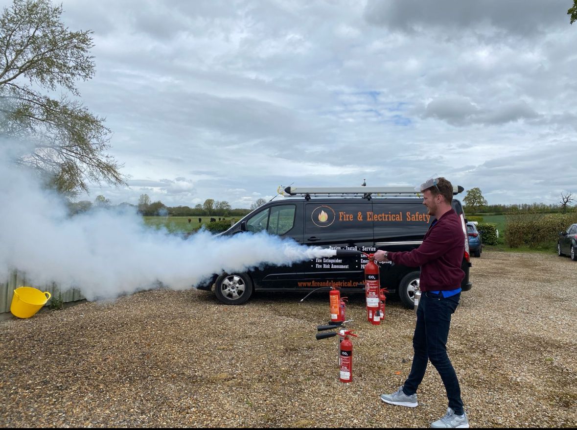 Person using a fire extinguisher during outdoor safety training, with safety van in the background.