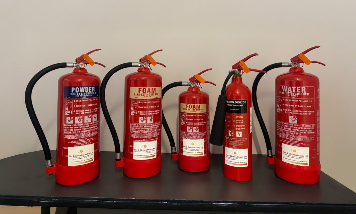 Five different types of fire extinguishers on a black table against a plain wall.