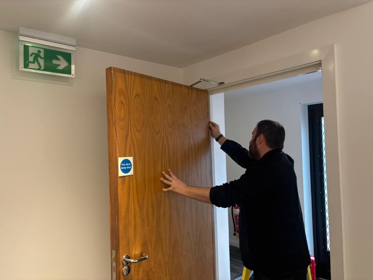 Man inspecting a fire door under an emergency exit sign in a hallway.