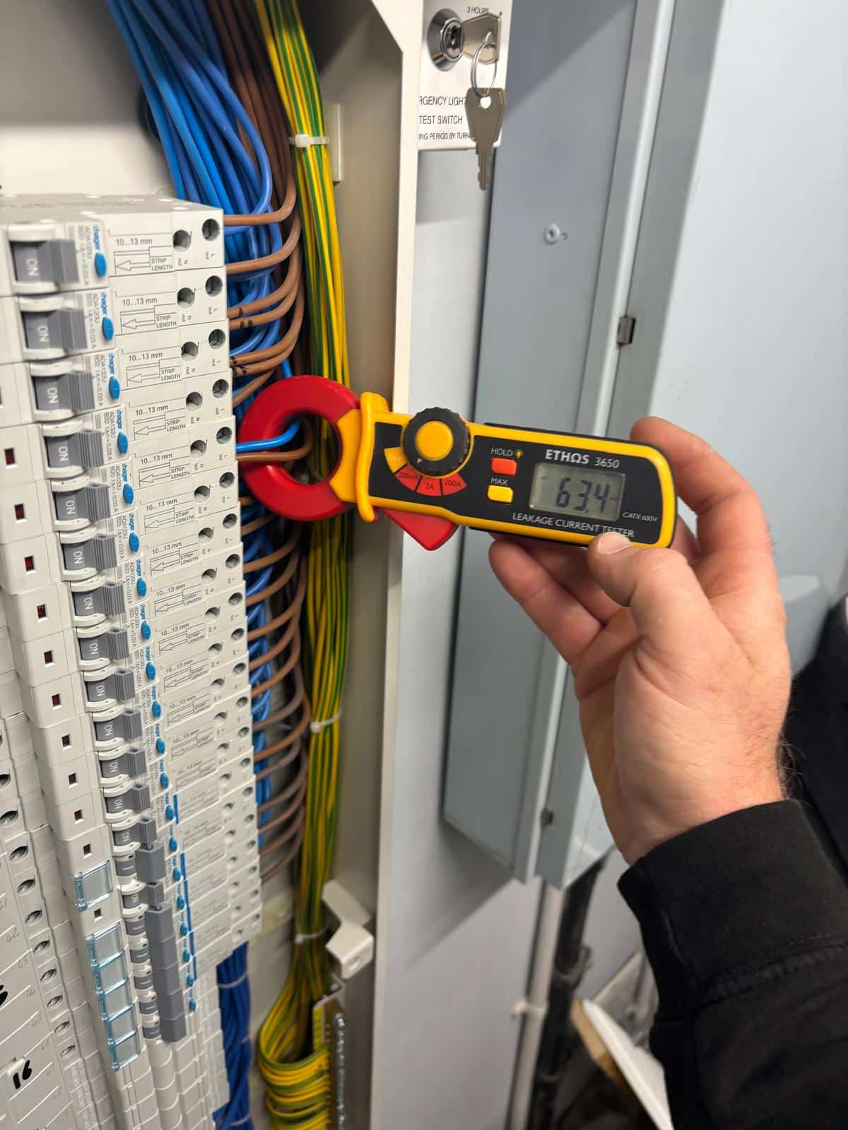 What is Electrical Testing A person tests wires in an electrical panel using a digital clamp meter.