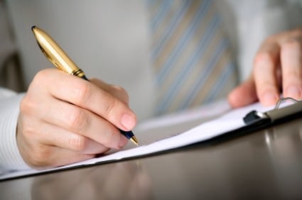 A person writing on a clipboard with a pen at a desk.