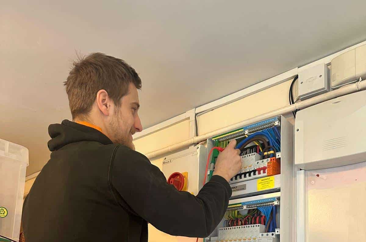 Why is testing important Man inspecting or testing electrical wires inside a control panel on a wall.
