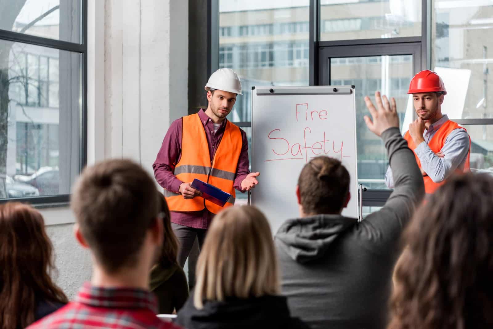 Fire safety training session with workers in safety vests and hard hats speaking to an audience.