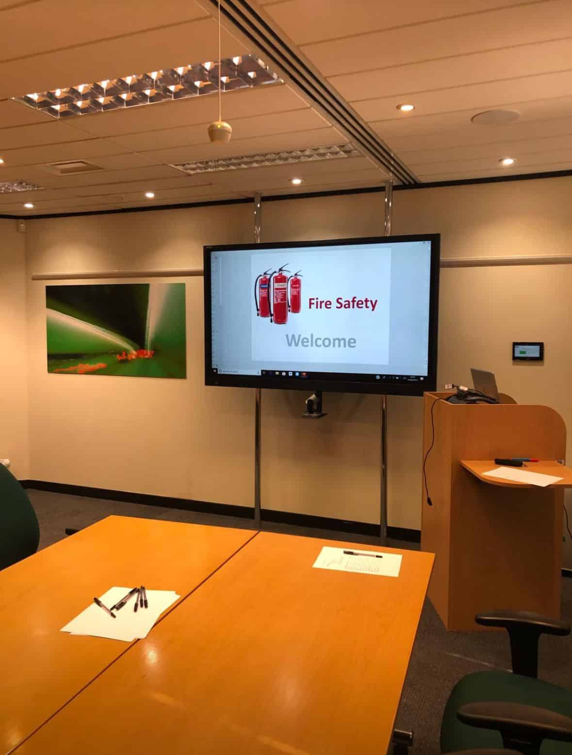 Meeting room set up for a fire safety training with a presentation screen and writing materials.